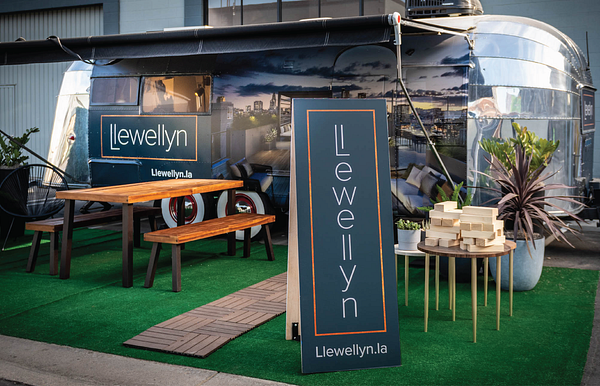 A free standing blue sign with the Llewellyn logo place on top of green turf with a picnic table slightly behind the sign and a food trailer in the background