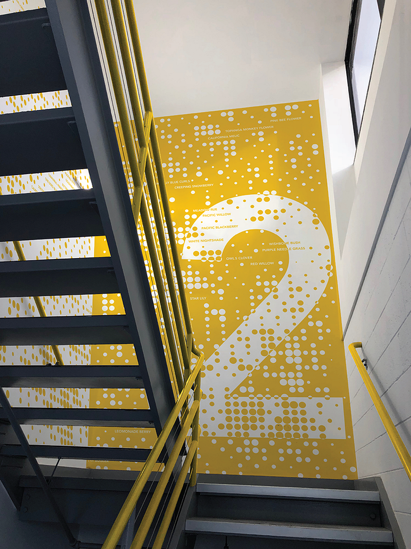 A yellow wall graphic of the number two with little circles making textures that's placed at the landing of stairs to mark the floor number.