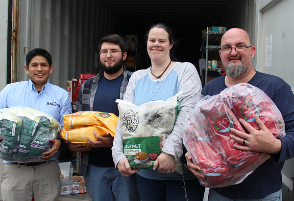 Volunteers stand with bags of pet food in hand while restocking the pet food pantry.