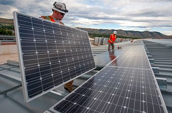 Men in hard hats install solar panels on rooftop with mountains in background