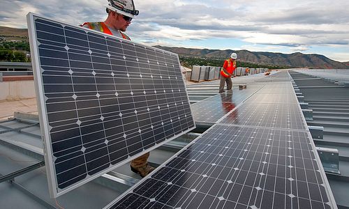 Men in hard hats install solar panels on rooftop with mountains in background