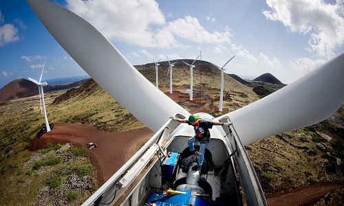 Man woking high in the air inside wind tubine moto, with other wind turbines in the background