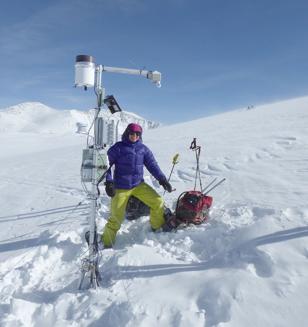 Woman next to soil monitoring equipment on snowy mountain pass