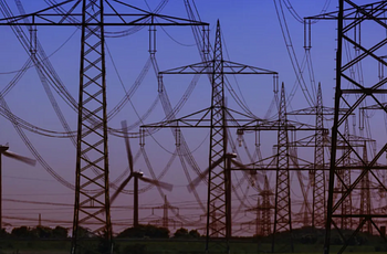 Electrical transmission towers with wind turbines in background at dusk