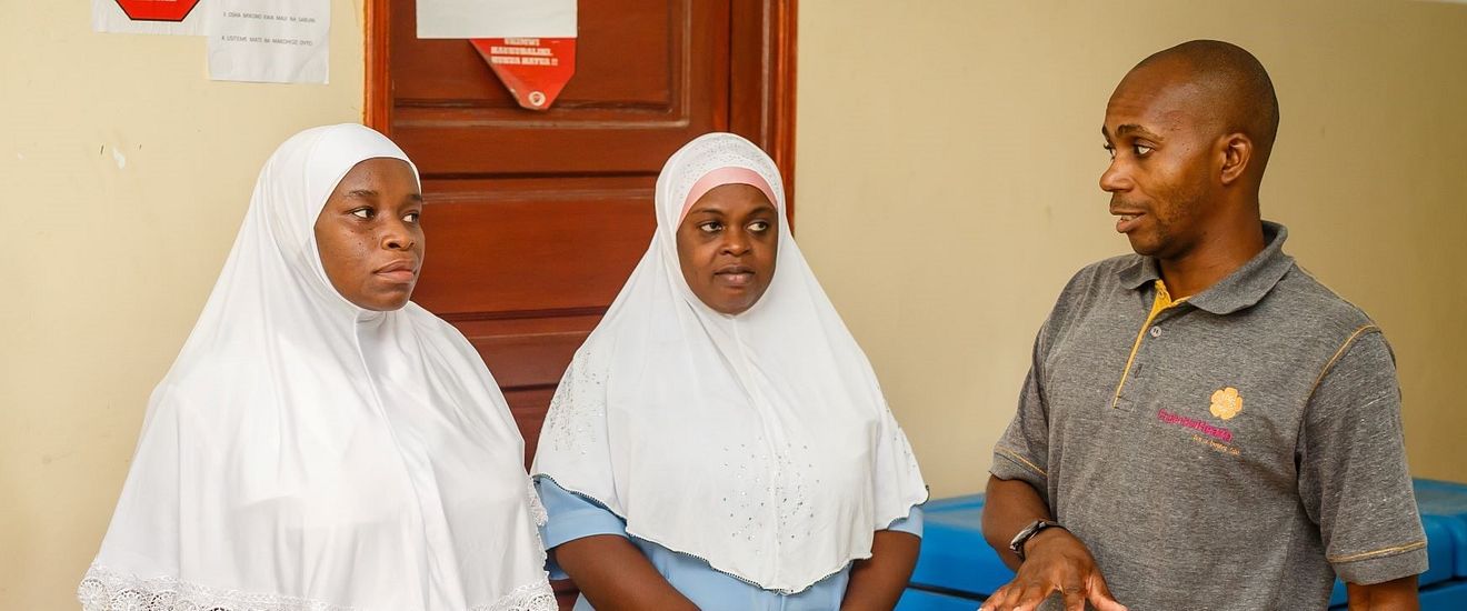 A man in an EngenderHealth polo speaks to two women wearing white headcoverings.