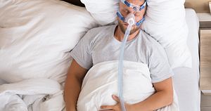Young,Man,Lying,On,Bed,With,Sleeping,Apnea,And,Cpap