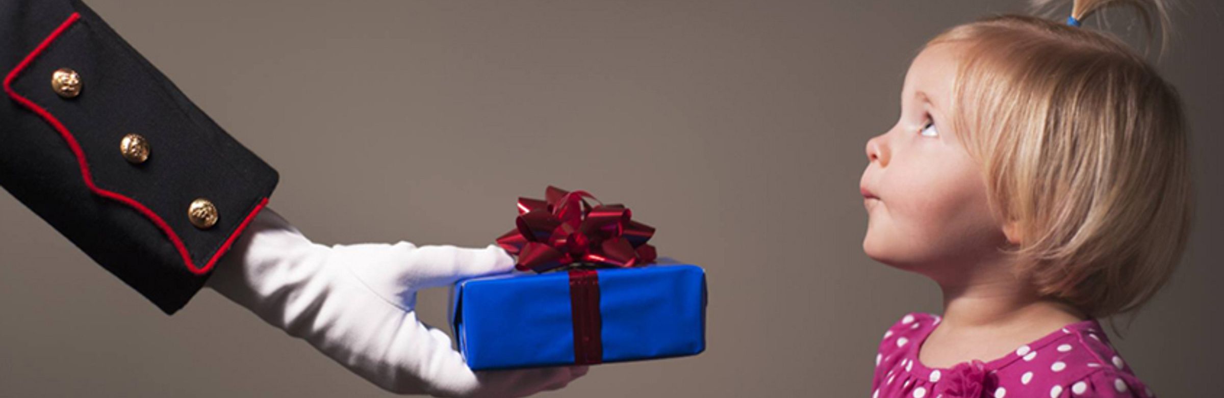The hand of a person in a full dress military uniform hands a wrapped present to a small child