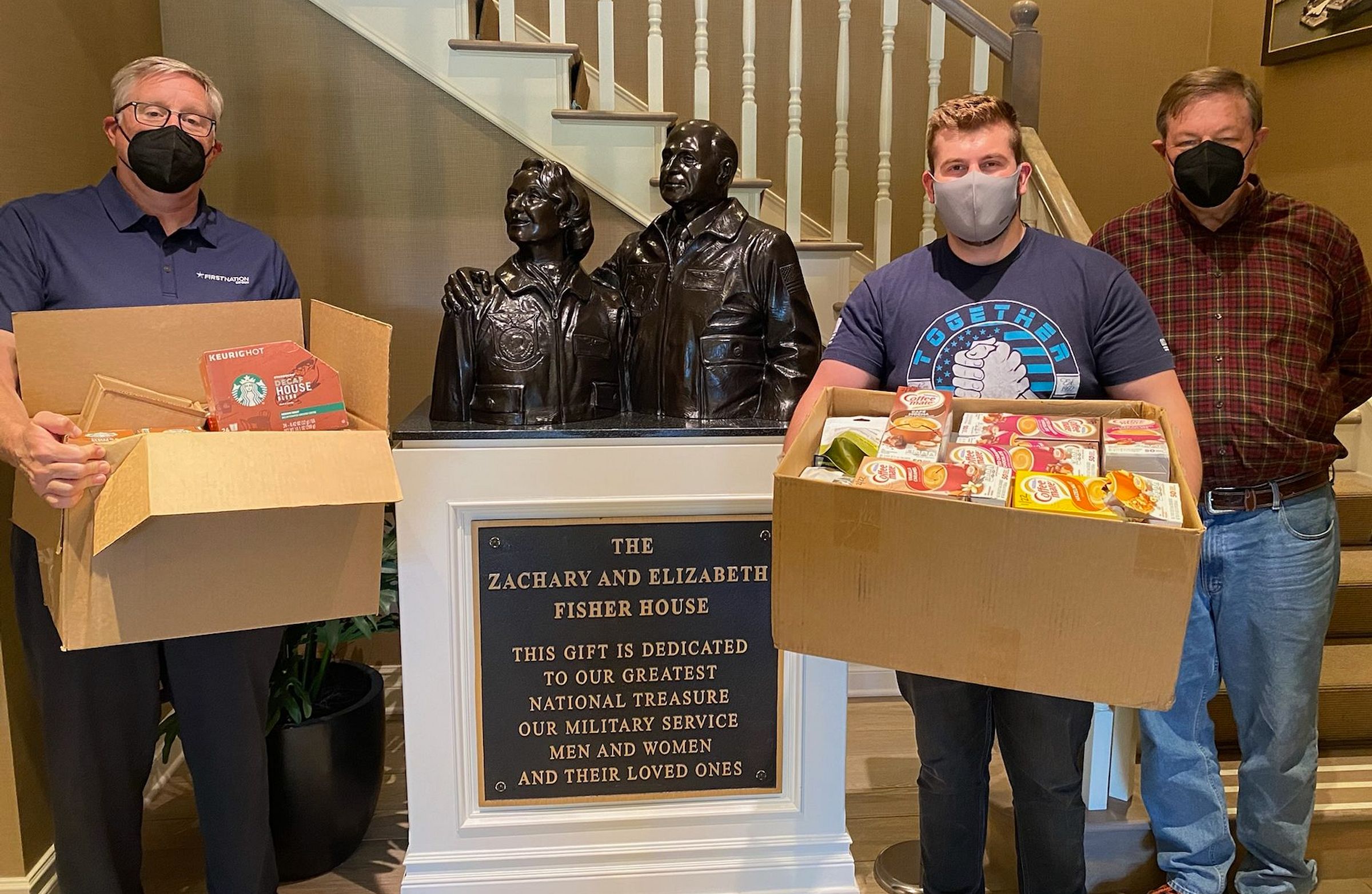 A group of three men hold large boxes of donations and pose for a photo