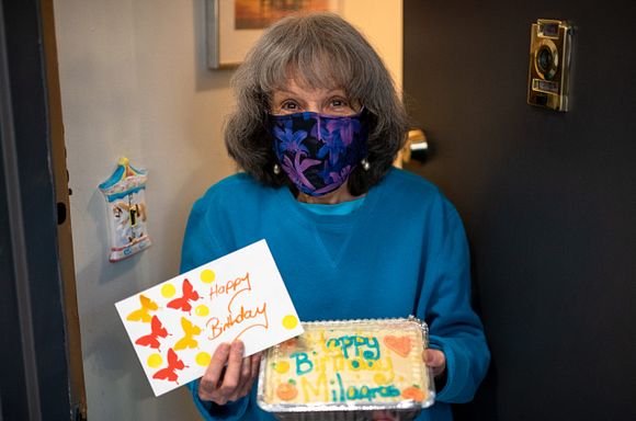 A photo of client, Milagros, holding a birthday cake and card at her door.