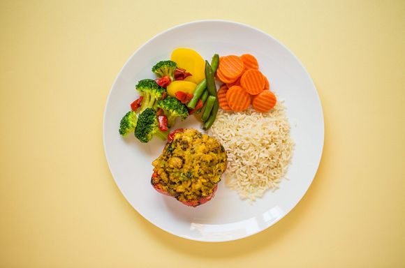 White bean stuffed red peppers on a plate with rice, carrots and mixed vegetables.