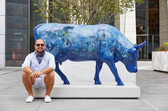 Photo of artist, Chris Sainato, sitting in front of his CowParade NYC cow sculpture.