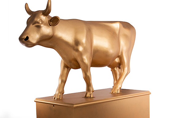 Left facing entire cow is gold on top a gold pedestal.