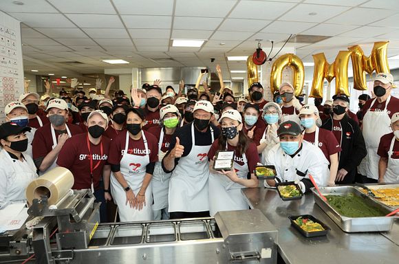Hugh Jackman, Sutton Foster, Karen Pearl, God's Love staff and volunteers in maroon shirts and masks holding up the 30 millionth meal in the kitchen