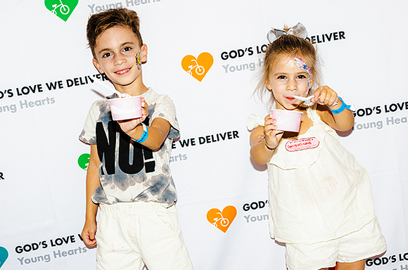 A photo of two children smiling and enjoying ice cream in front of the Young Hearts step & repeat.