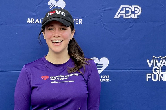 A photo of Maura smiling in front of a step & repeat after finishing the Race to Deliver.