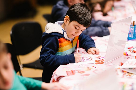 A photo of a child with short black hair decorating colorful cards at a table.