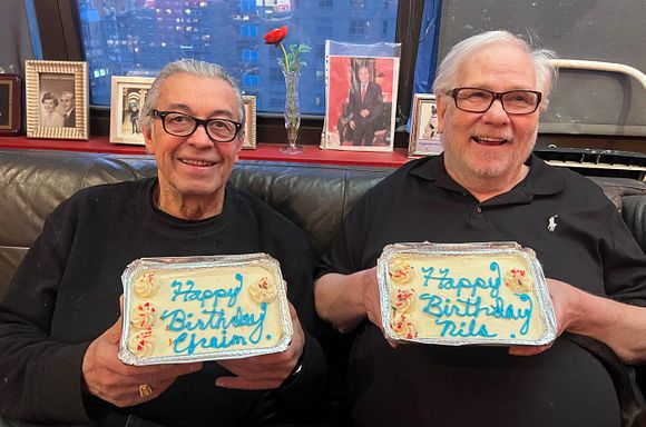 Clients Nils and Efraim sitting together on their couch, holding personalized birthday cakes, smiling