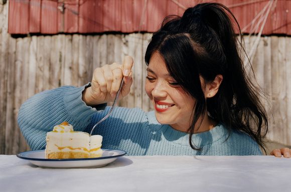 A photo of chef Natasha Pickowicz smiling while cutting into a slice of cheesecake with a fork.