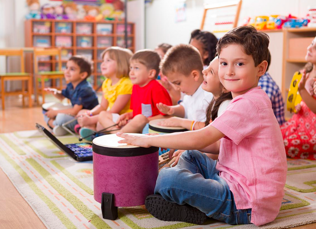 Group of diverse young children playing different musical instruments during a music class.