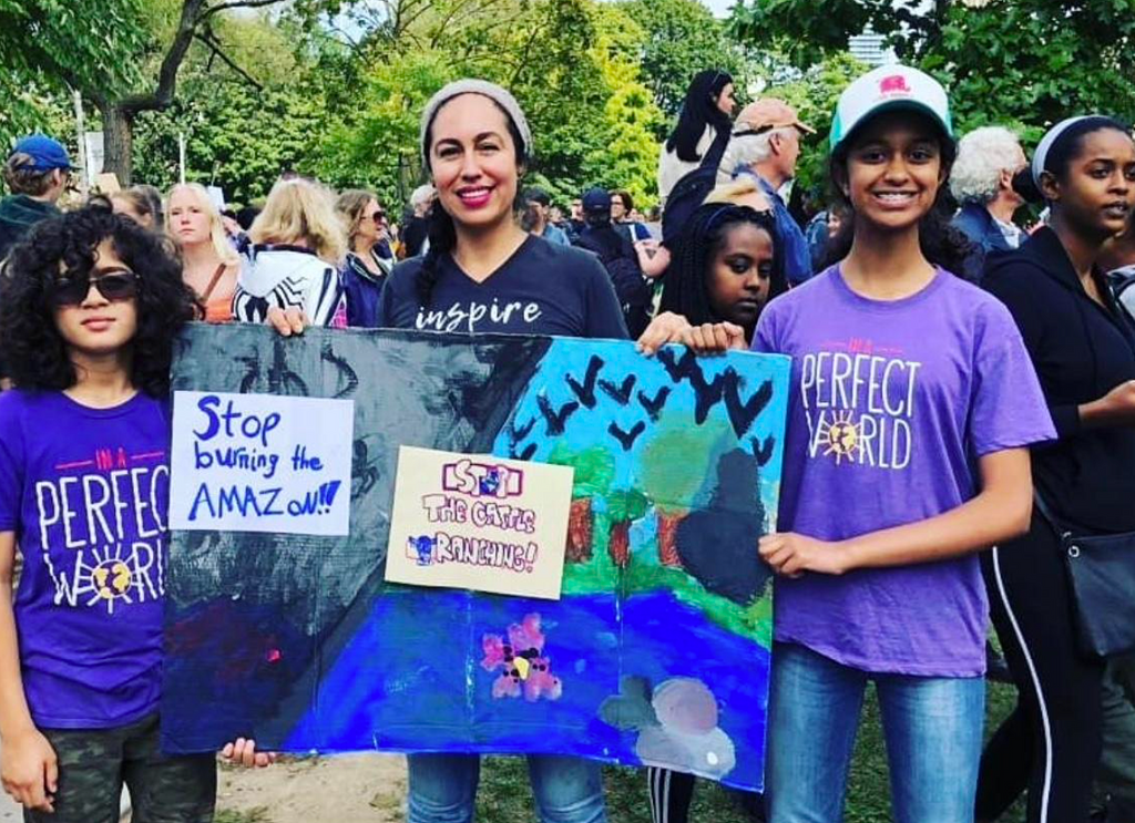 Two multi-ethnic teens holding a sign at a protest with their female teacher - empowering youth leadership in the community.