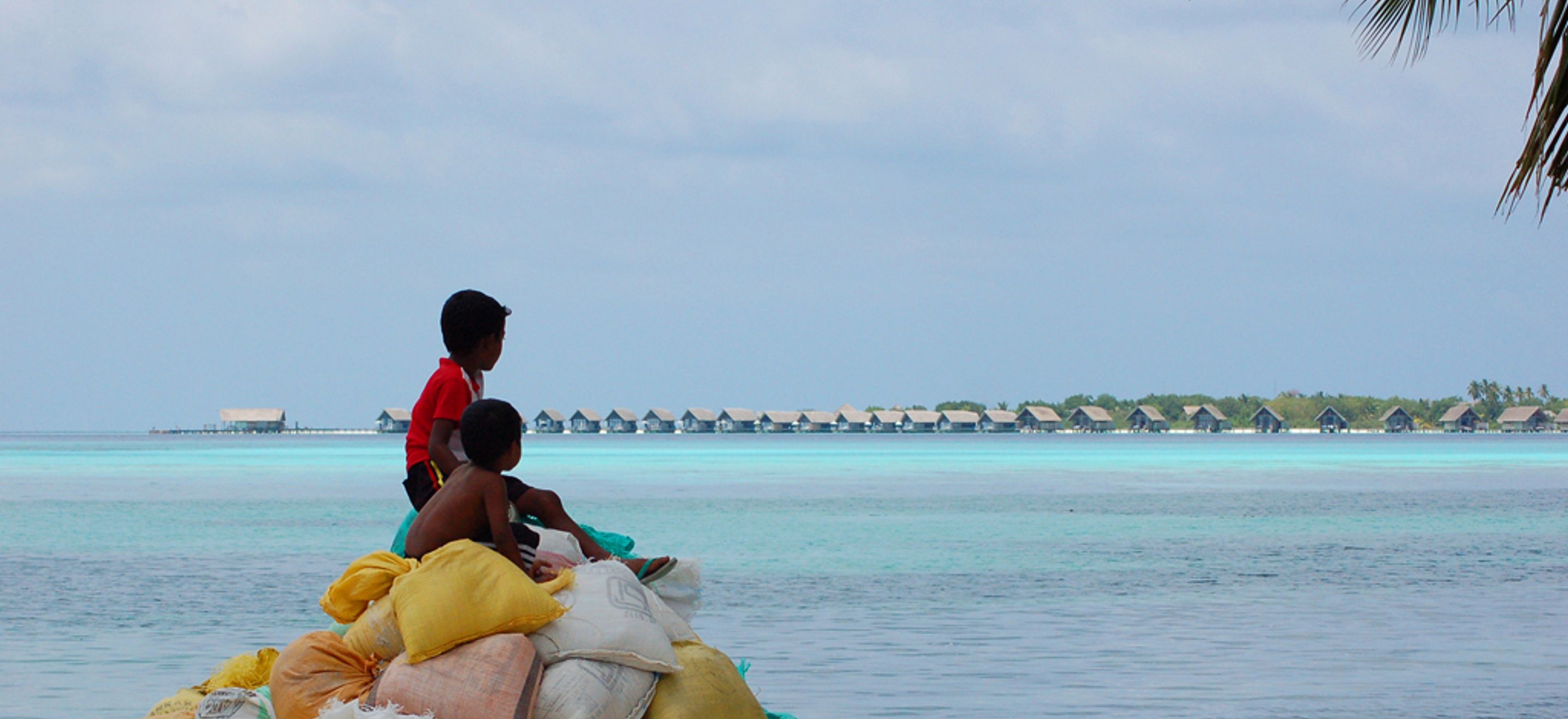 Two children sitting on bags look across the sea to an adjacent island.