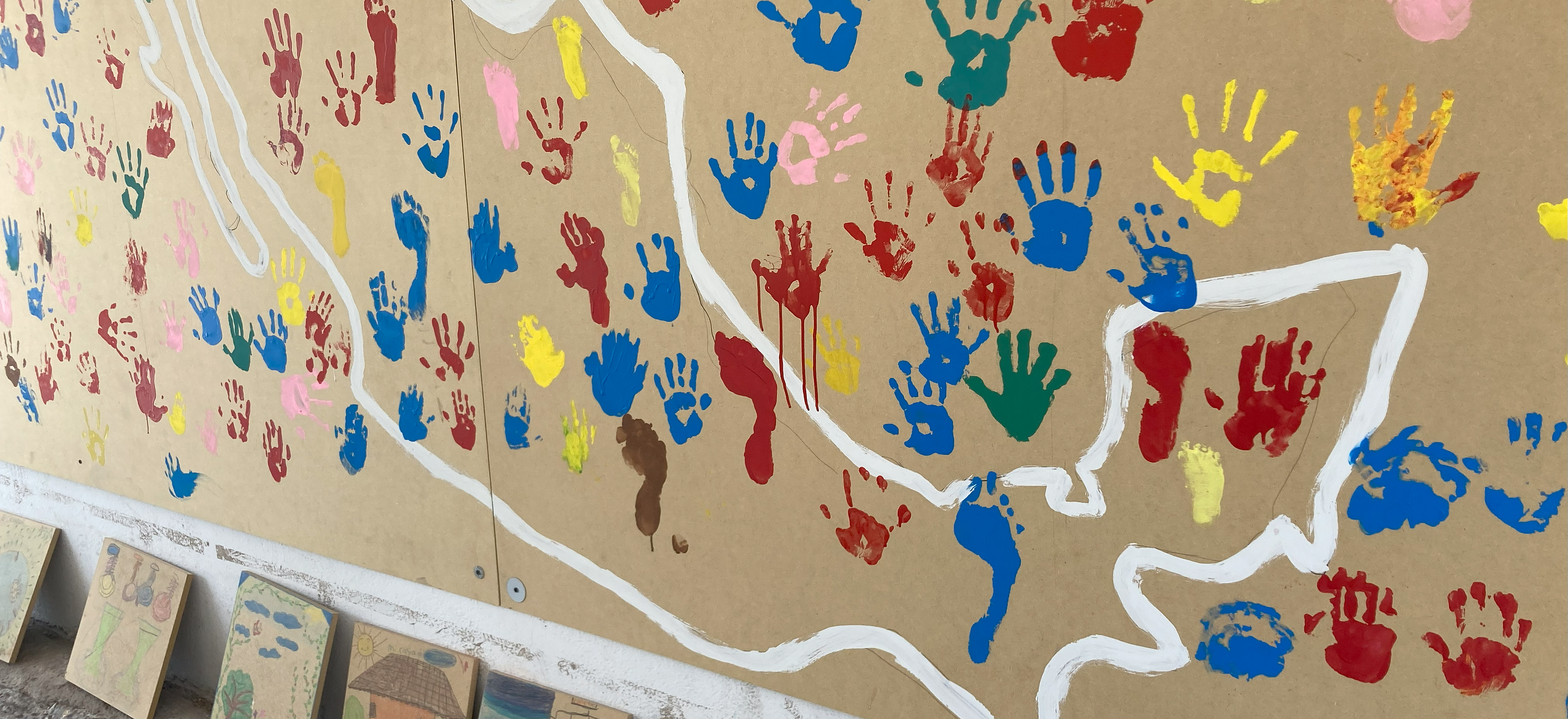 A photo of a children's mural project with handprints in different color paint across an outline of Mexico.