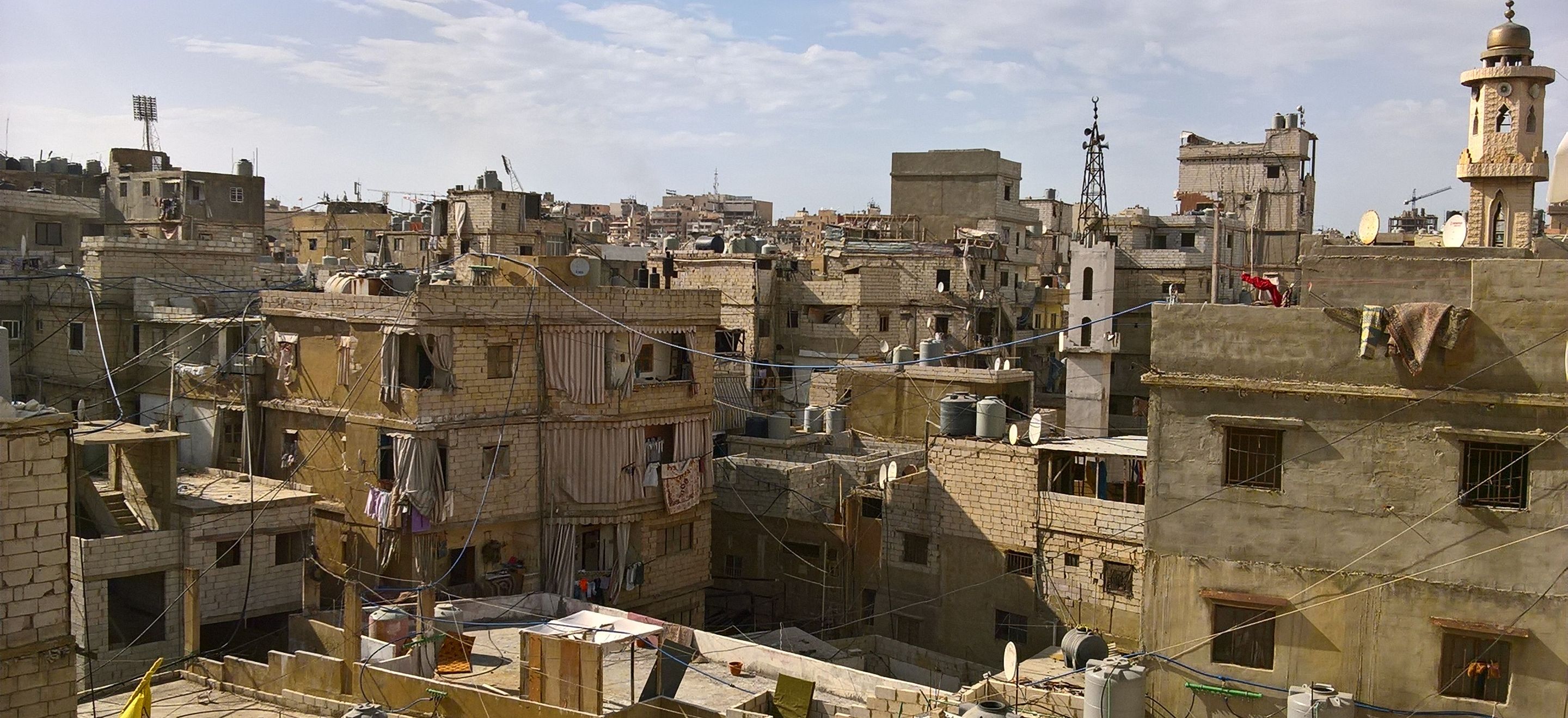 An image of the southern Beirut skyline from the Shatila refugee camp. There are many cinderblock buildings with electrical wires running from roof to roof.