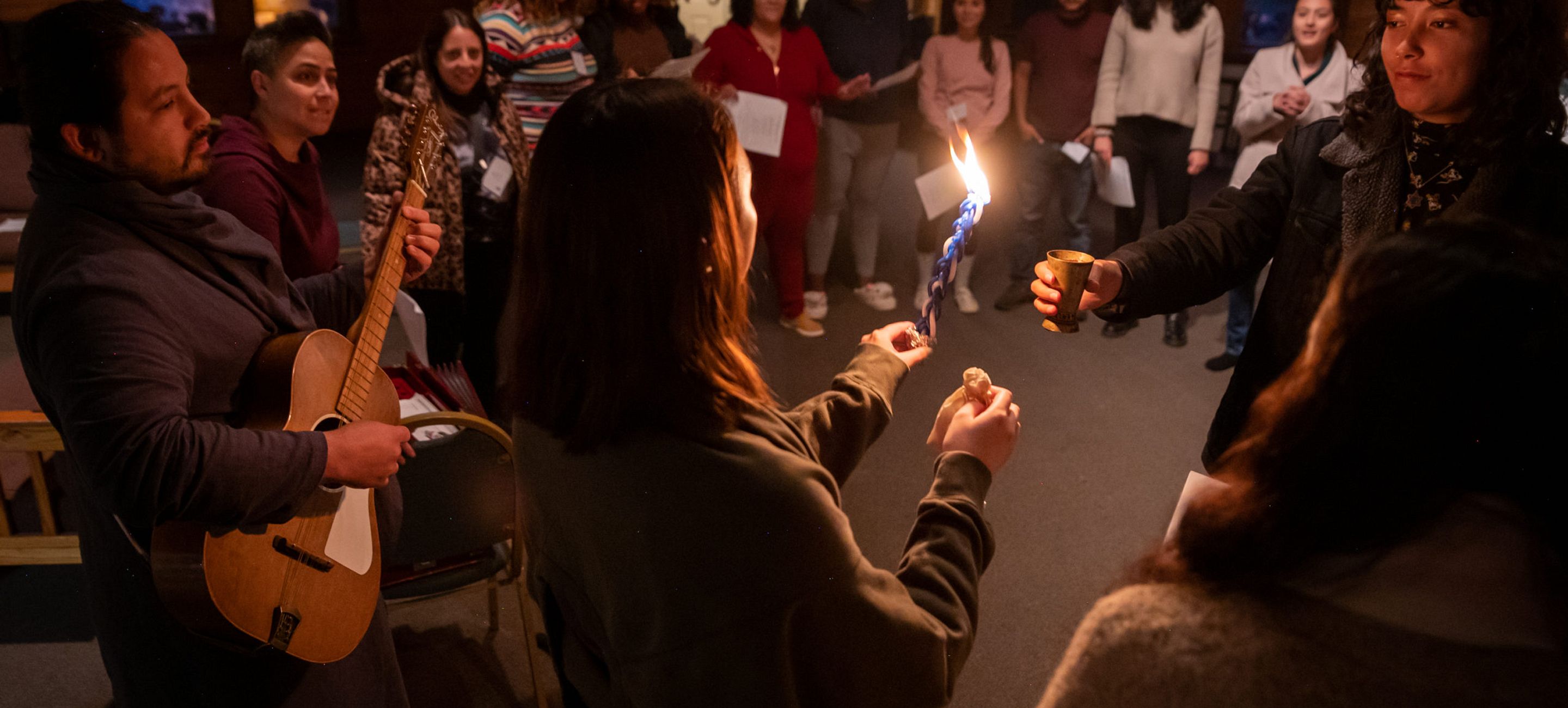 Young adult woman lights a candle with others in a circle