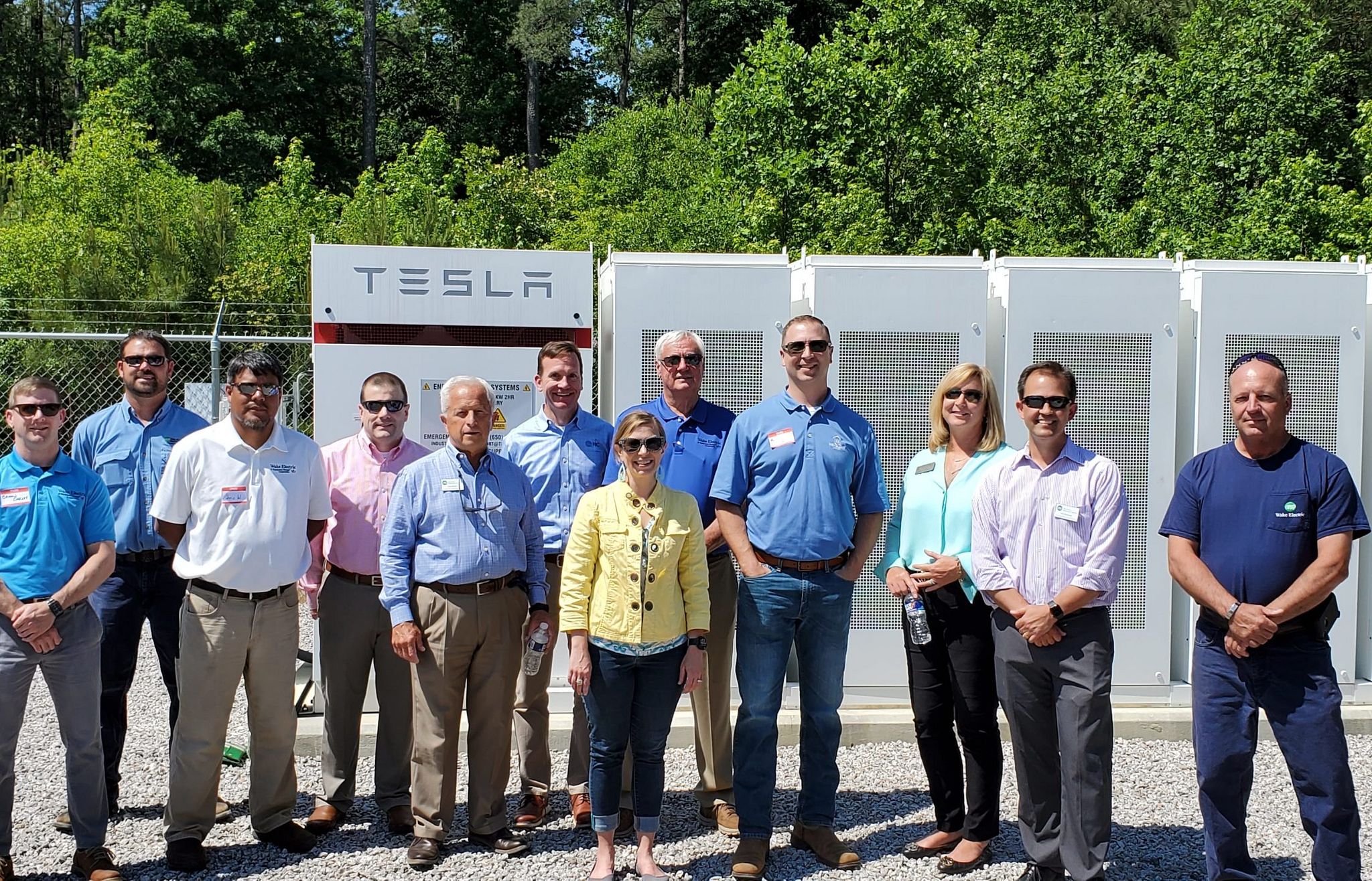 A crowd stands in front of a large bank of Tesla batteries on the site of the Eagle Chase microgrid