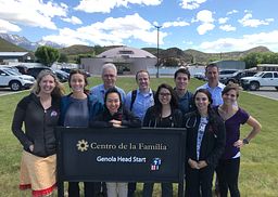 Students and faculty from the Utah PA Program stand in front of an exterior sign at the Centro de la Familia Genola Head Start Program