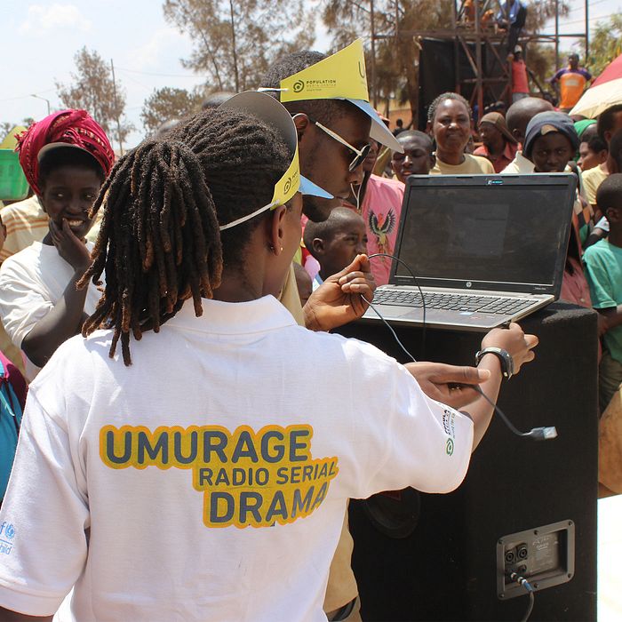 Woman wearing an "Umurage" t-shirt sets up a computer while working in front of an event crowd.