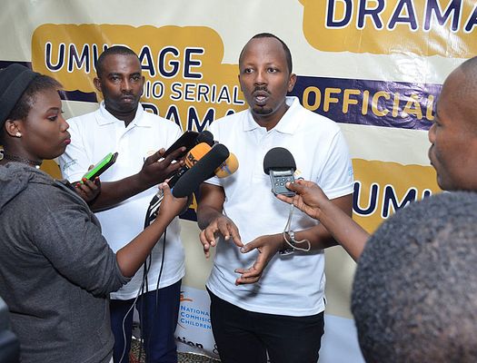 Man interviewed with multiple microphones with the Umurage logo in the background