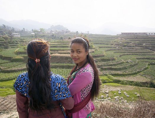 Two Nepalese women with their arms around each other as they look down from a hill