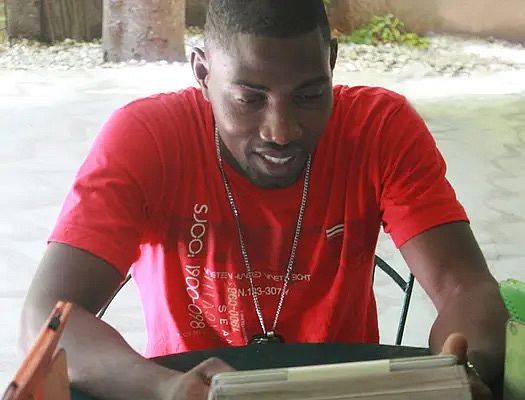 A Haitian man in a red shirt looks at a book