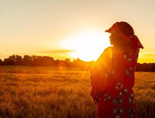 A woman stands in a field while the sun sets