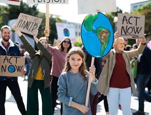 A group of protests march with signs. a young girl holds up a poster of the earth