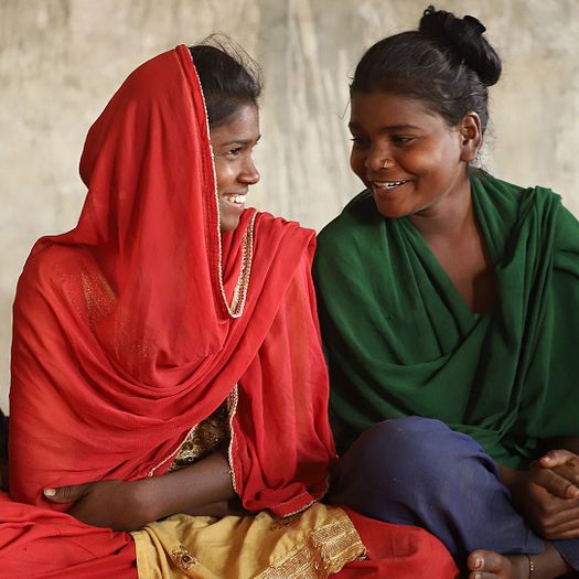 Nepali girls sitting together on the ground smiling at each other.