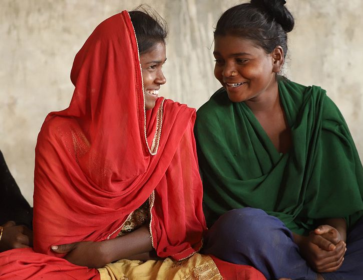 Nepali girls sitting together on the ground smiling at each other.