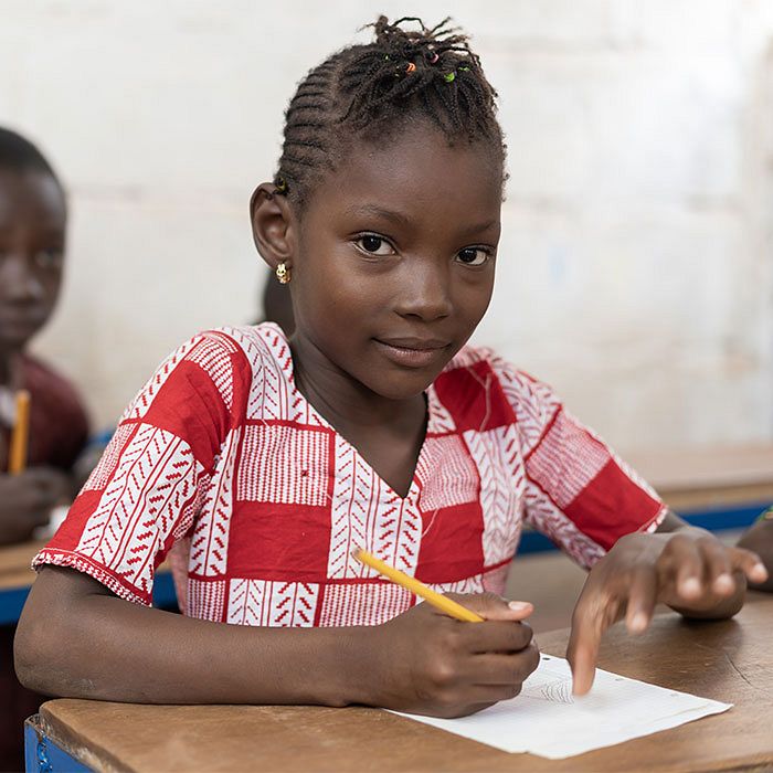 Girl child sits at a school desk with a pencil in her hand ready to continue her work.