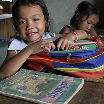 Photo of a classroom desk, a young girl child leans over her backpack onto the table