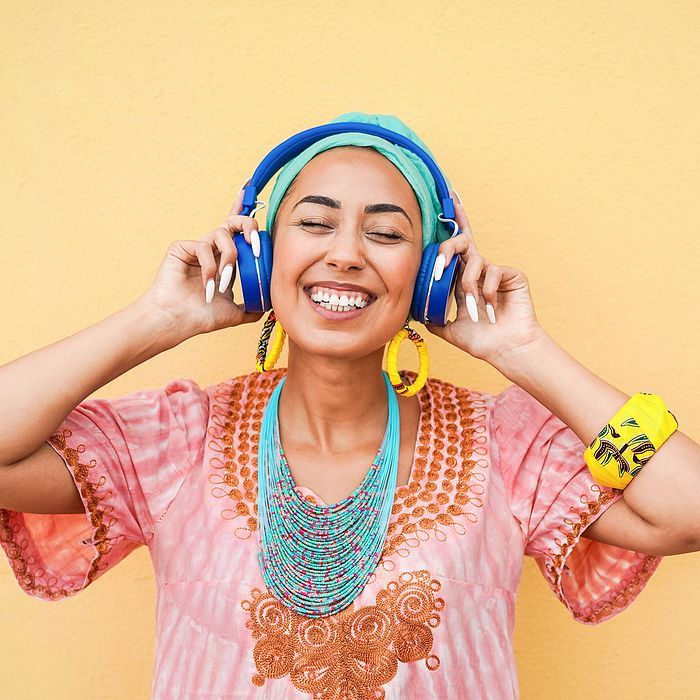 Woman listening to blue headphones. She has a huge smile and looks extremely joyful