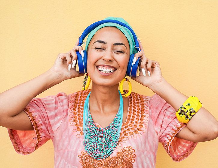 Woman listening to blue headphones. She has a huge smile and looks extremely joyful