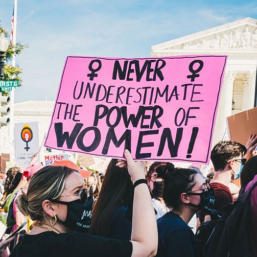 Women's march in front of the US Supreme court. A woman holds a pink sign that reads, "Never underestimate the power of women!"