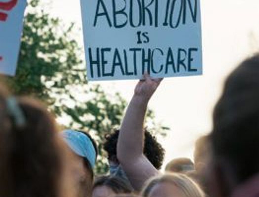 Hand holds sign up above a crowded protest group. The sign says 'abortion is healthcare'