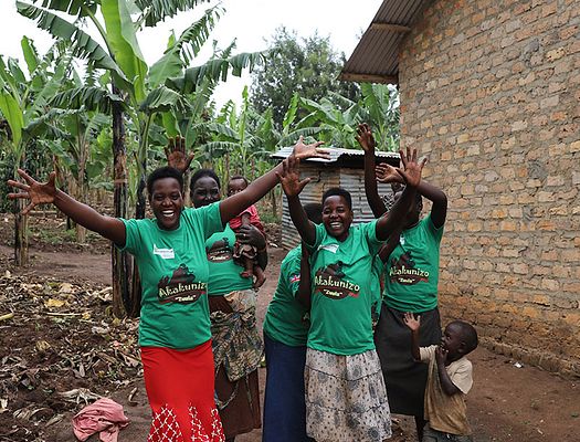 A group of people wearing green Akakunizo tshirts celebrate with their hands in air and big smiles on their faces.