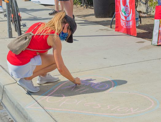 Girl writes 'End All Oppression' with chalk on the sidewalk