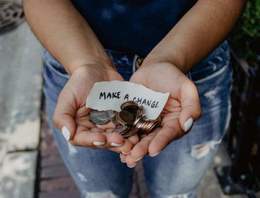 a woman holds coins in her hand with a slip of paper saying "Make a Change"