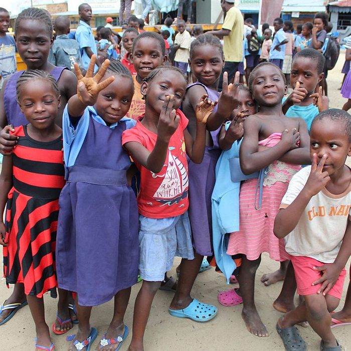 Children huddled together for a picture showing the peace sign, thumbs ups, and other hand signals.