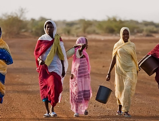 Five women walk through a dirt plain