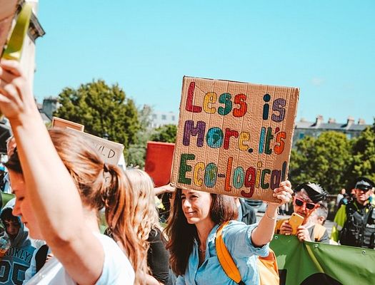 A cardboard sign that says "Less is More. It's Eco-logical
